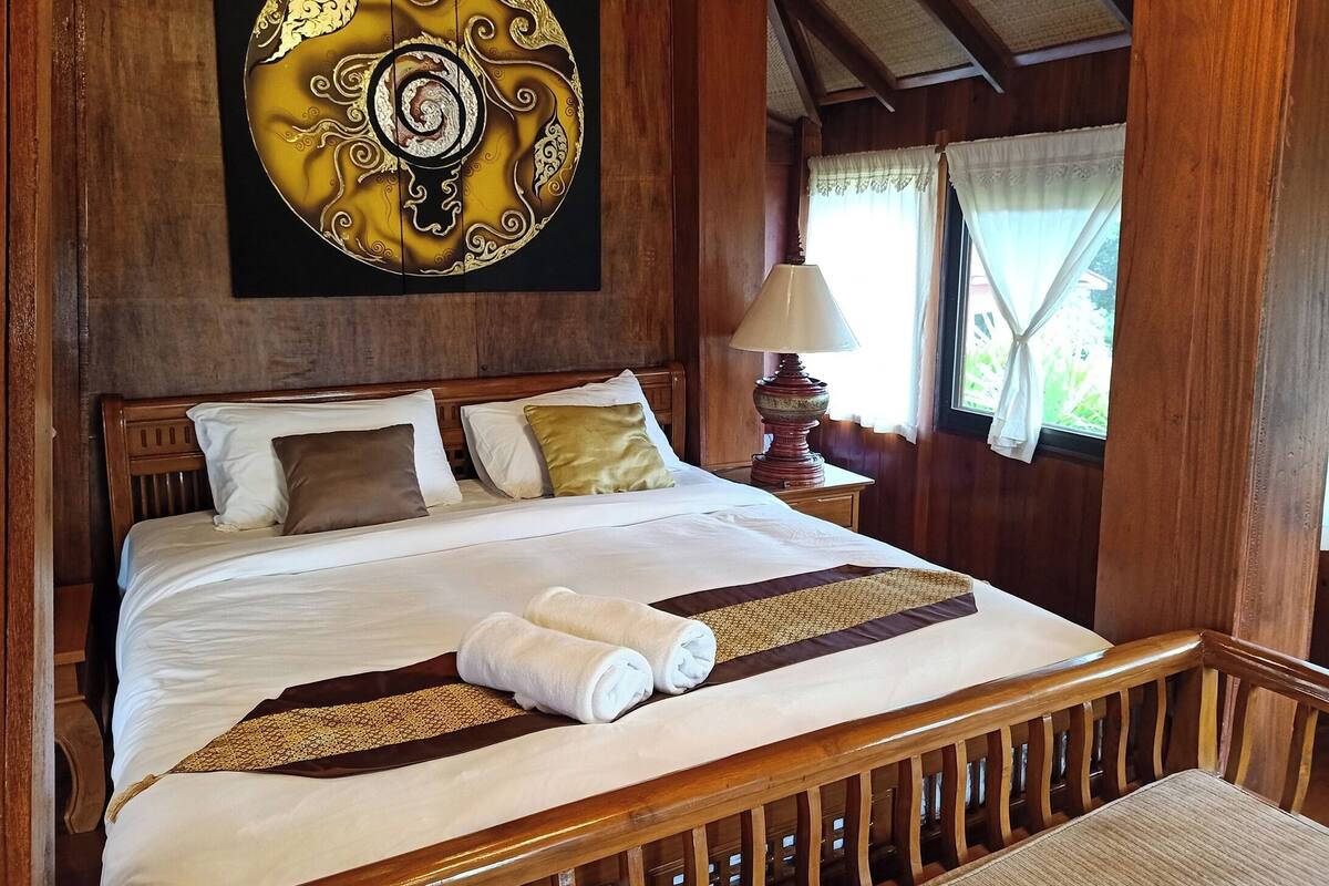 Una cama bien hecha con sábanas blancas y un corredor decorativo marrón, un cabecero de madera y una obra de arte colgada en la pared.