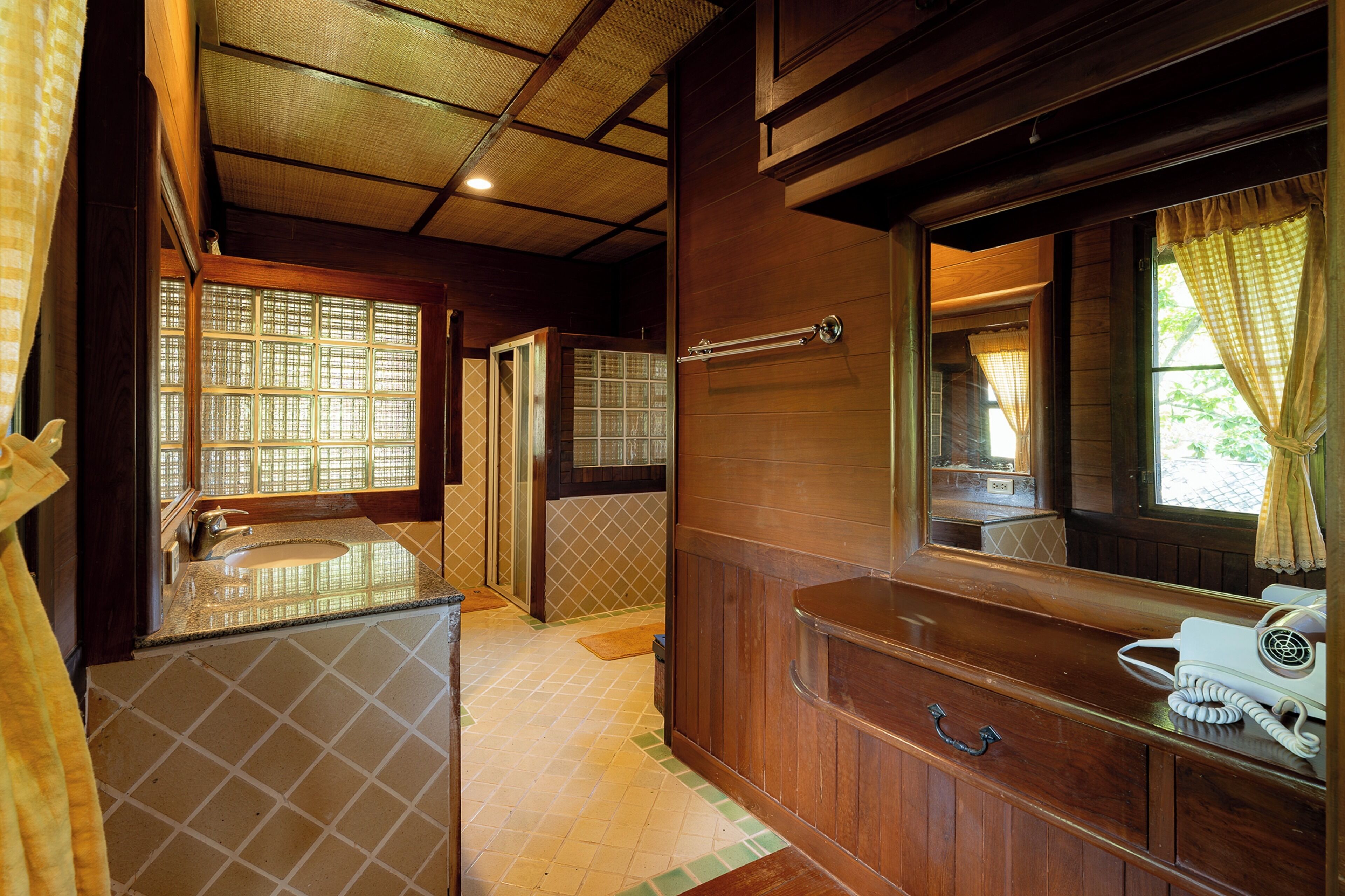 A bathroom with a wooden vanity, a mirror, and a window with curtains.