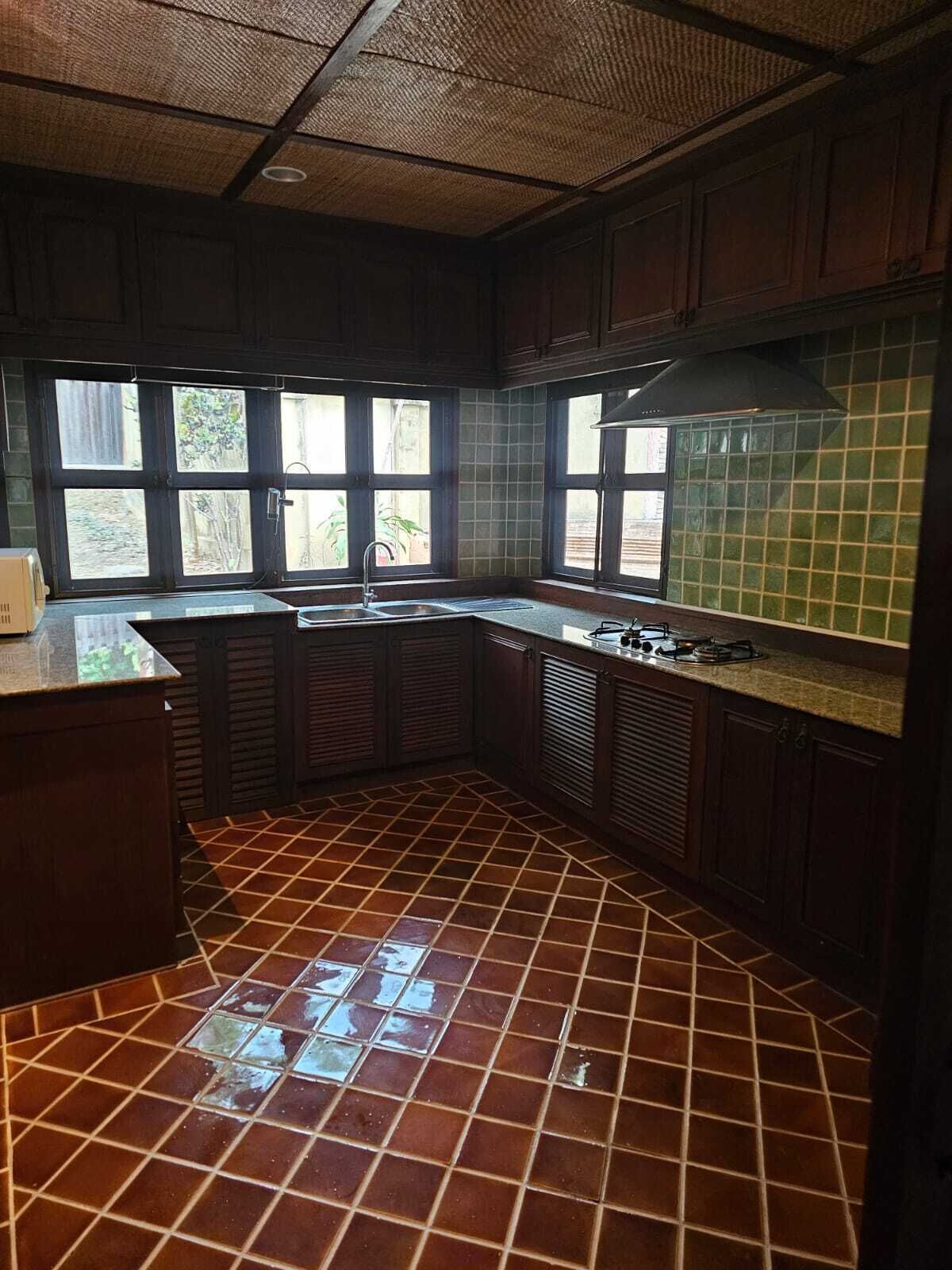 Una cocina con piso de baldosas, estufa a gas, un lavamanos y un ventanal con vistas a zonas verdes.