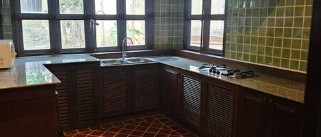 Una cocina con piso de baldosas, estufa a gas, un lavamanos y un ventanal con vistas a zonas verdes.