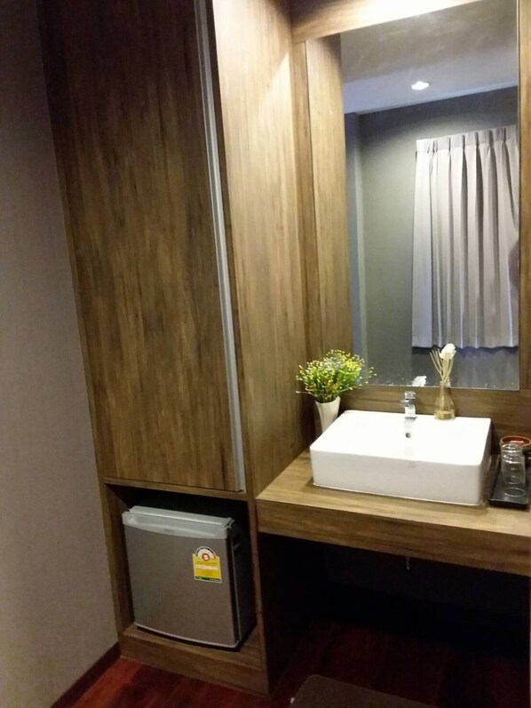 A modern bathroom with a wooden vanity, a white sink, and a small trash bin.