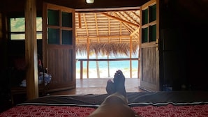 Quarto com cama, porta de madeira que dá para uma varanda com vista para a praia.