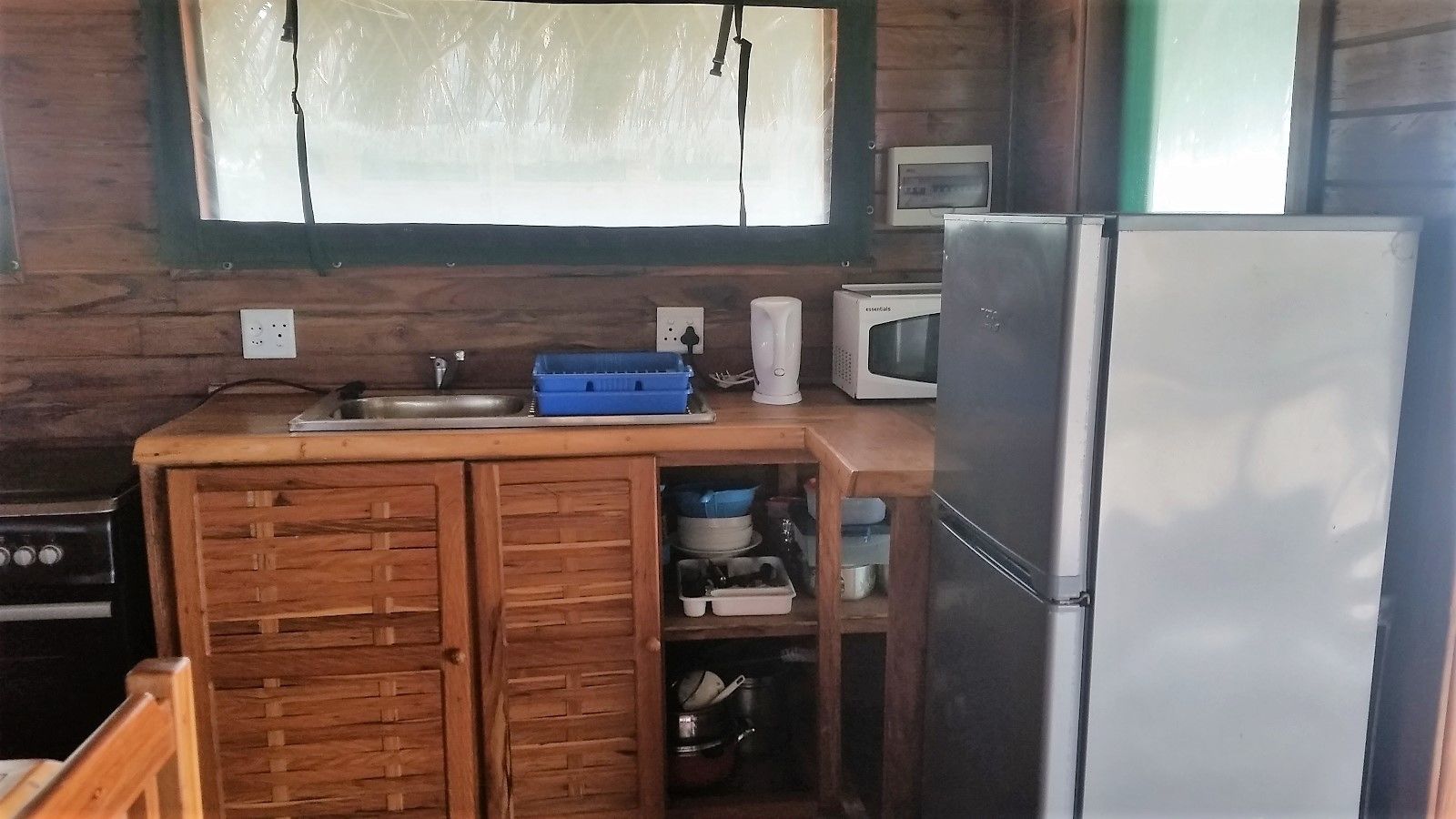 A compact kitchen with wooden cabinets, a stainless steel refrigerator, a microwave, and a sink.