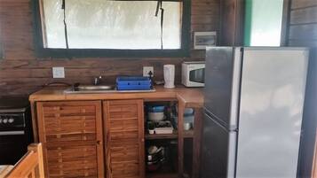 A compact kitchen with wooden cabinets, a stainless steel refrigerator, a microwave, and a sink.