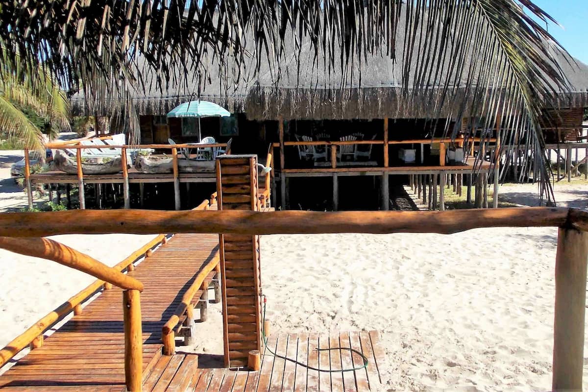 A wooden deck leading to a thatched-roof building with a view of the beach.