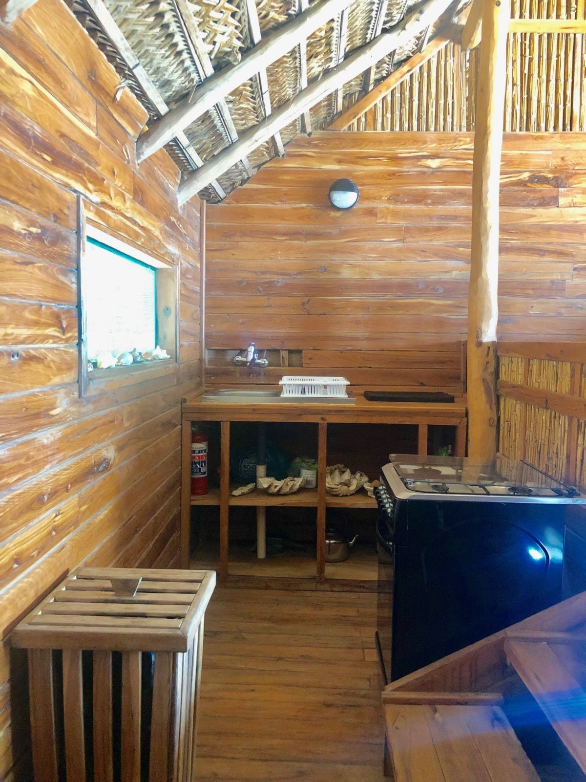 A wooden cabin interior with a kitchen area, including a stove, sink, and a window with a view.