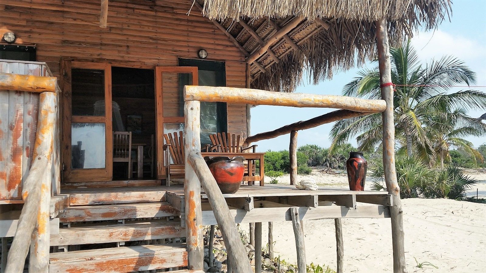 Un bâtiment en bois avec un toit de chaume, une véranda en bois et un grand pot placé sur la véranda.