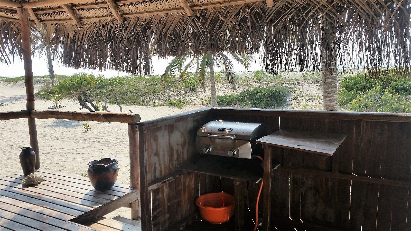 Una parrilla de madera bajo una estructura de techo de paja en la playa.