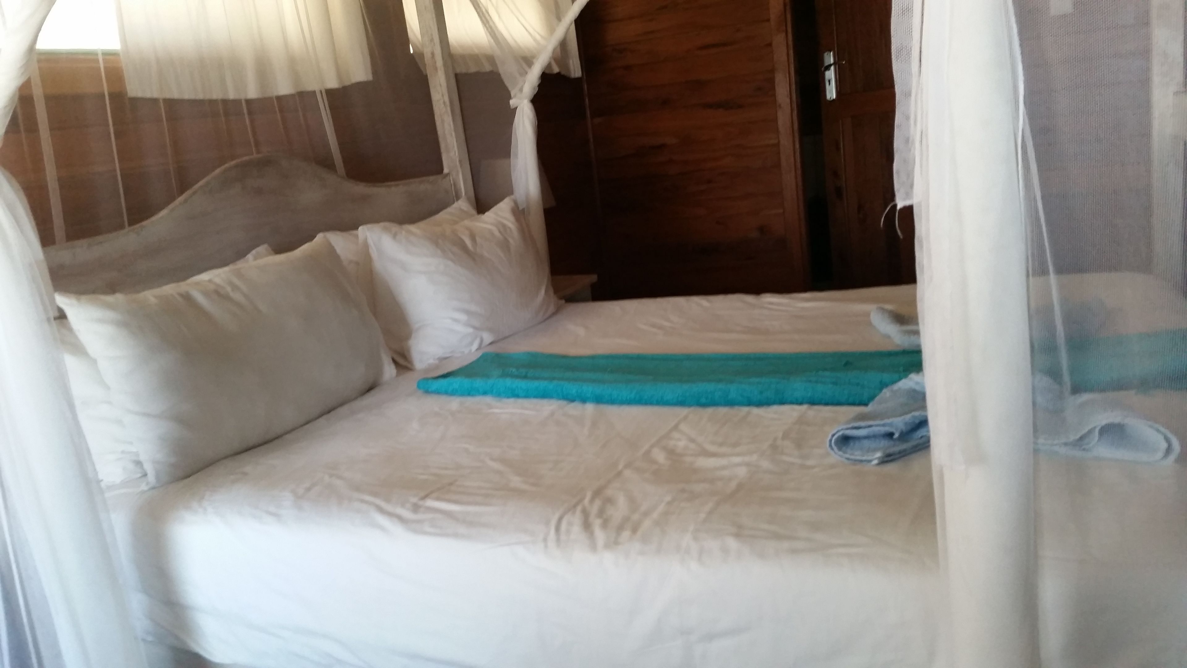 Uma cama com lençóis brancos, uma toalha azul e um mosquiteiro.