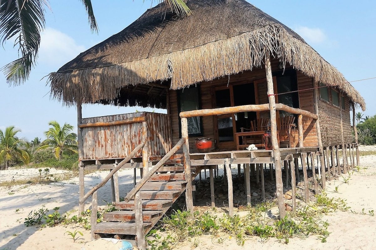 A wooden structure with a thatched roof, a wooden porch, and a staircase leading to a deck.