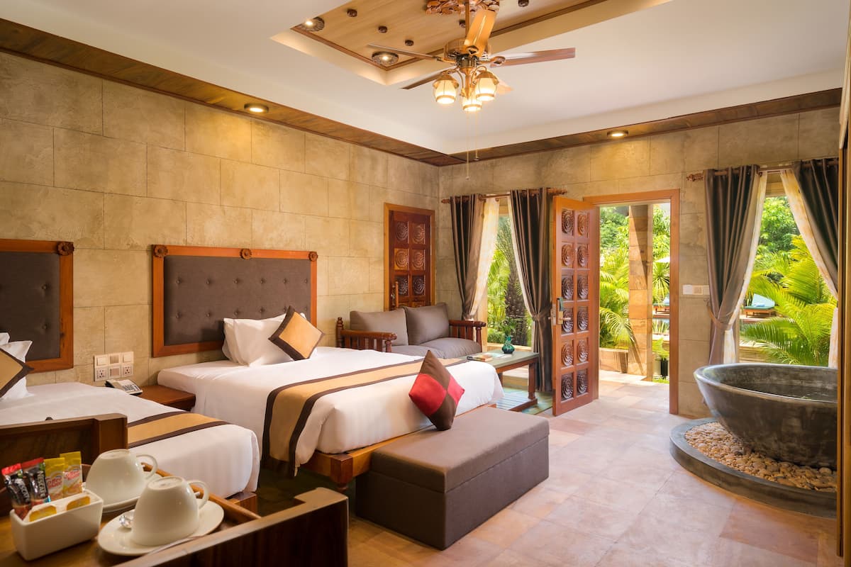 A hotel room with two beds, a large window, a ceiling fan, and a view of the garden.