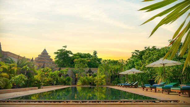 A pool area with lounge chairs and umbrellas, surrounded by lush greenery and a temple structure. - Model Residence and Spa (Siem Reap)