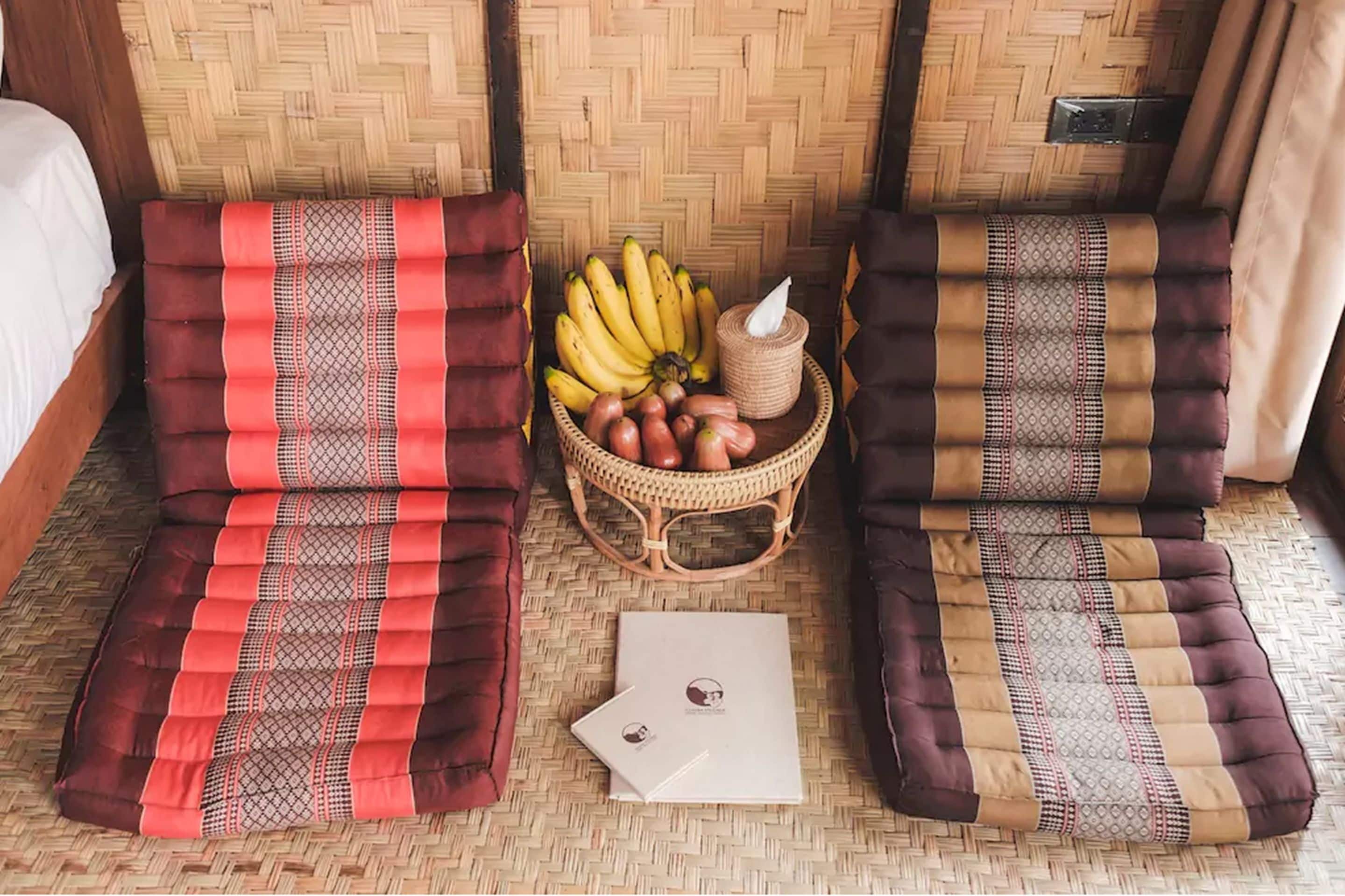 Une pièce avec deux fauteuils rembourrés, un panier en osier contenant des bananes et des pommes, et un livret blanc posé sur le sol.