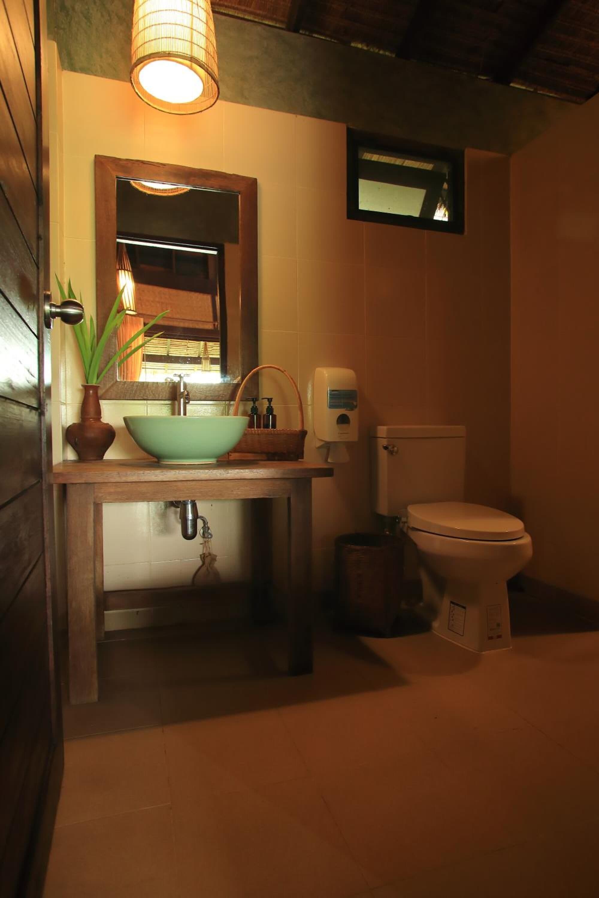 Une salle de bain avec un meuble-lavabo en bois, un lavabo vert, un miroir, des toilettes et une petite fenêtre.