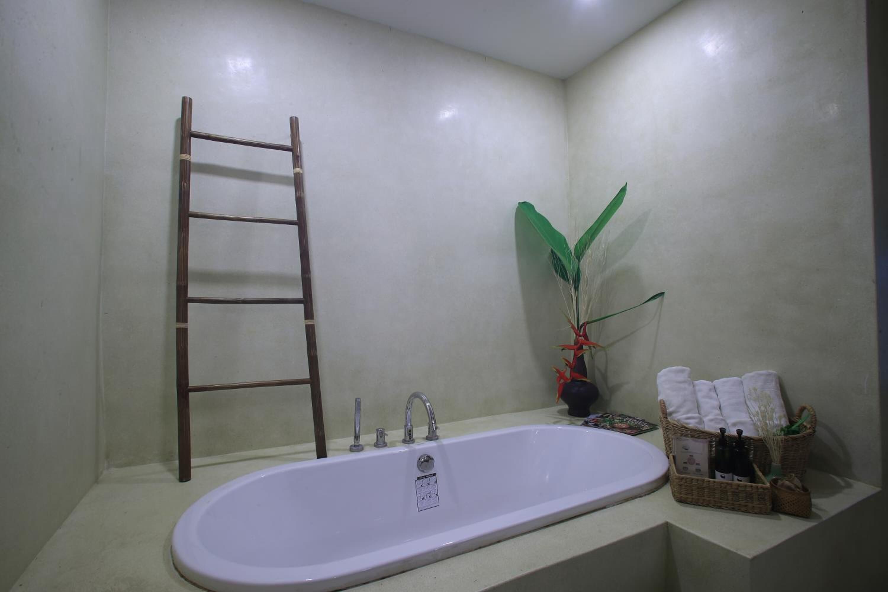 Une salle de bain avec une baignoire sur pieds, une échelle en bois, une plante en pot et un panier rempli de serviettes.