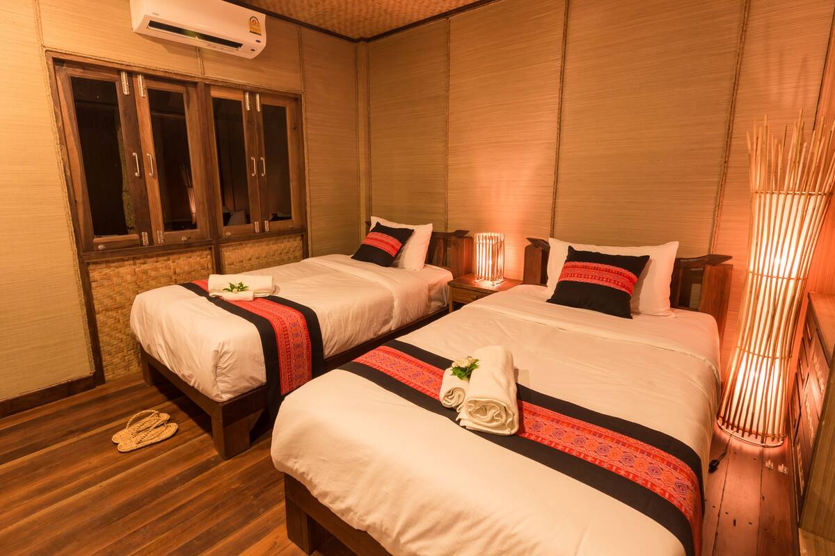Two single beds with white linens, red and black decorative pillows, and a wooden floor.