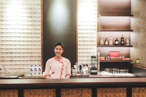 A bar area with a counter, shelves with bottles, and a person standing behind the counter. - Azalea Village Wellness Resort (Chiang Dao)