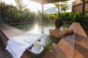 A person relaxing in a wooden deck by a pool with a tray of tea and a cup, surrounded by lush greenery and a mountain view. - Azalea Village Wellness Resort (Chiang Dao)