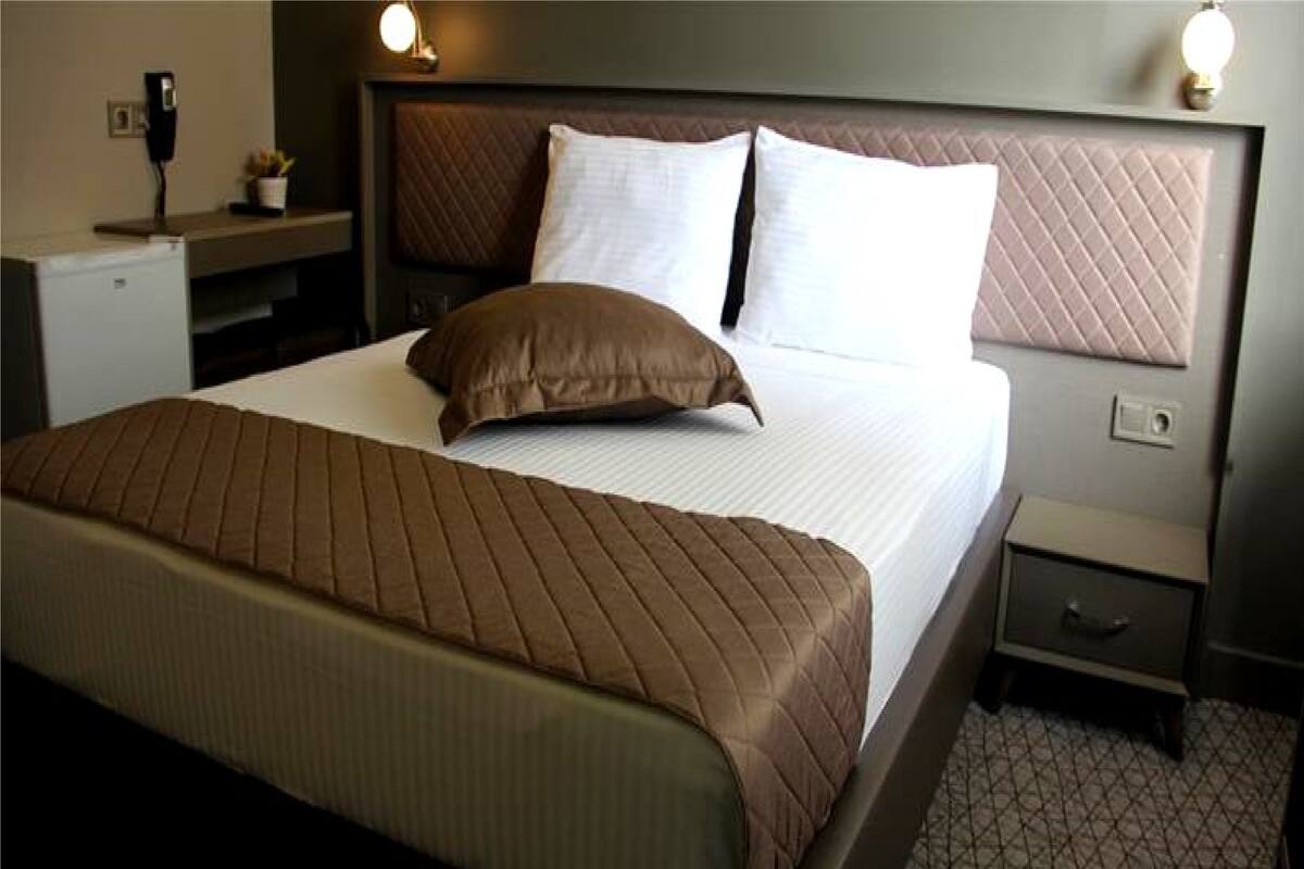 A neatly made bed with a brown quilt, a bedside table with a lamp, and a small nightstand with a lamp.