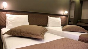 Habitación de hotel con dos camas, cada una con ropa blanca y almohadas marrones. Hay luces fijadas en la pared sobre las camas y un espejo en la pared.