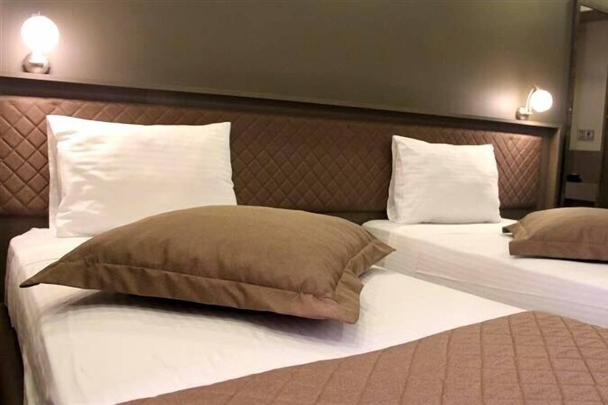 A hotel room with two beds, each with white linens and brown pillows. There are wall-mounted lights above the beds and a mirror on the wall.