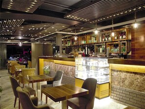 A restaurant with wooden tables and chairs, a bar area with shelves of bottles, and a display case with food items. - Turkeli Hotel (Istanbul)