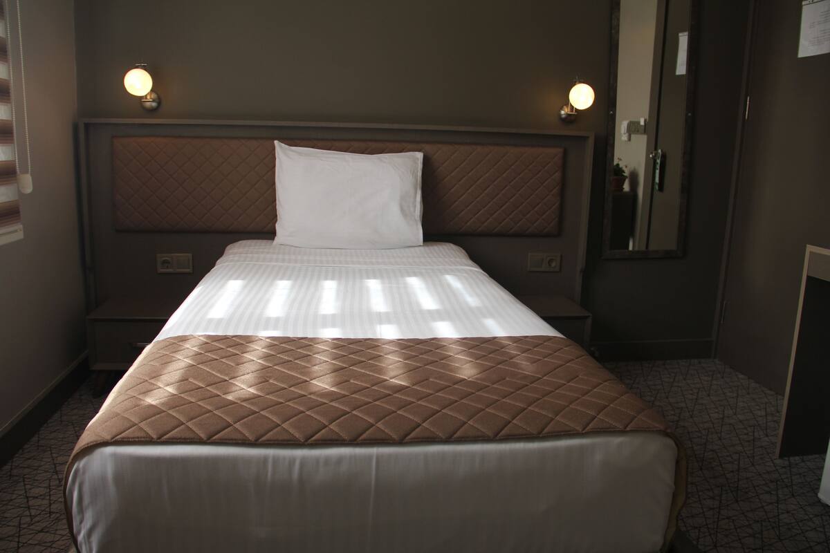 A hotel room with a queen-sized bed, a headboard with a quilted pattern, bedside lamps, a nightstand, and a mirror on the wall.