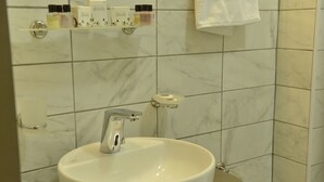 Un baño con lavamanos blanco, inodoro y repisa con artículos de aseo.