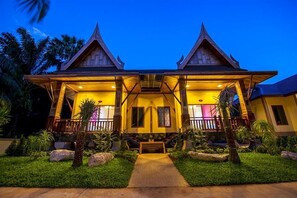 A traditional building with a central porch and two side wings, surrounded by tropical landscaping.