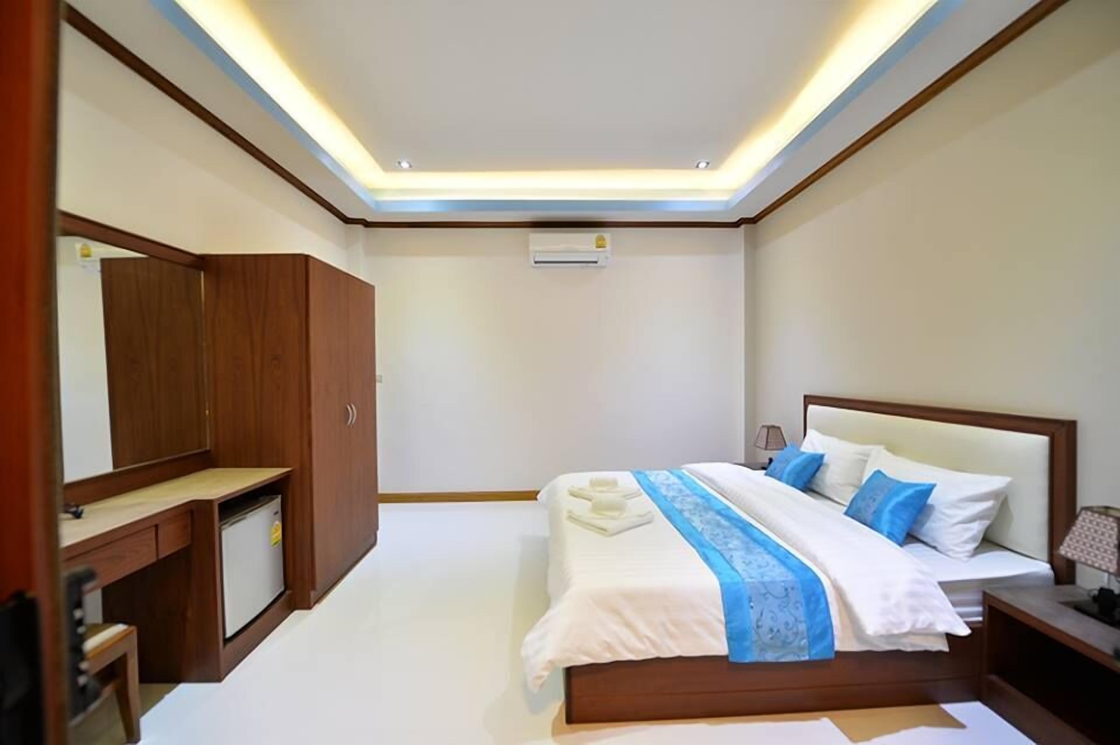 A hotel room with a bed, bedside table, nightstand, wardrobe, and built-in air conditioning unit.