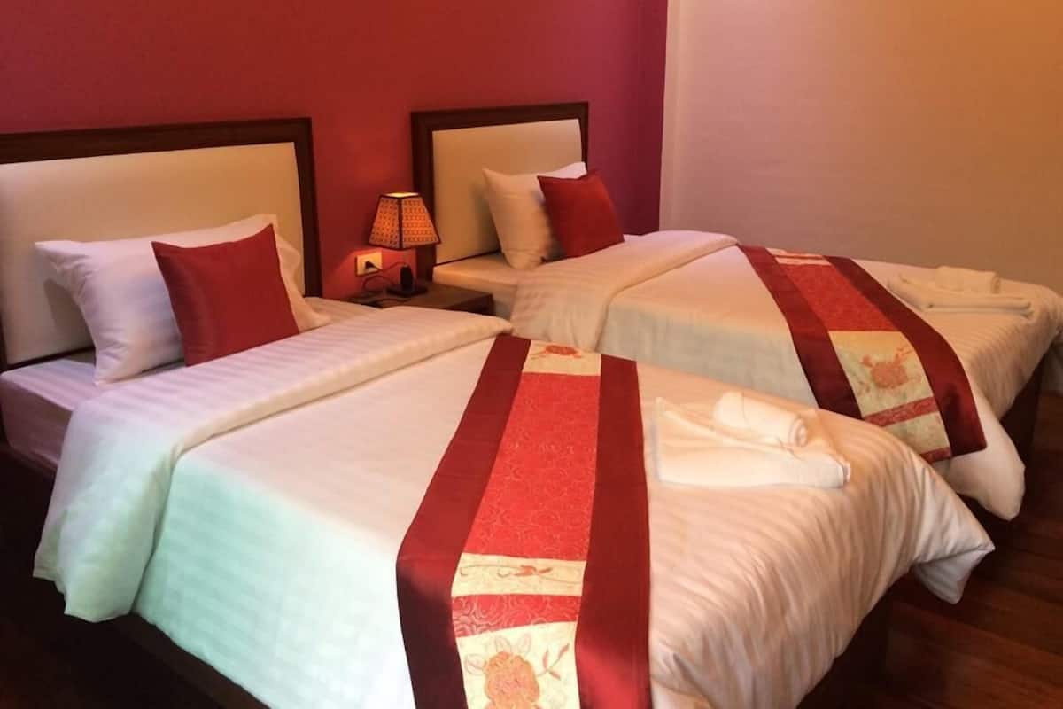 A hotel room with two beds, each with white linens and red decorative pillows.