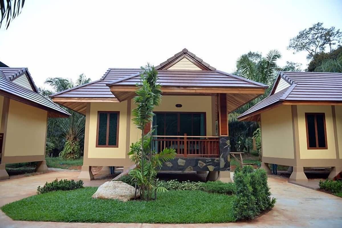 A row of two-story houses with a central porch, surrounded by greenery and palm trees.