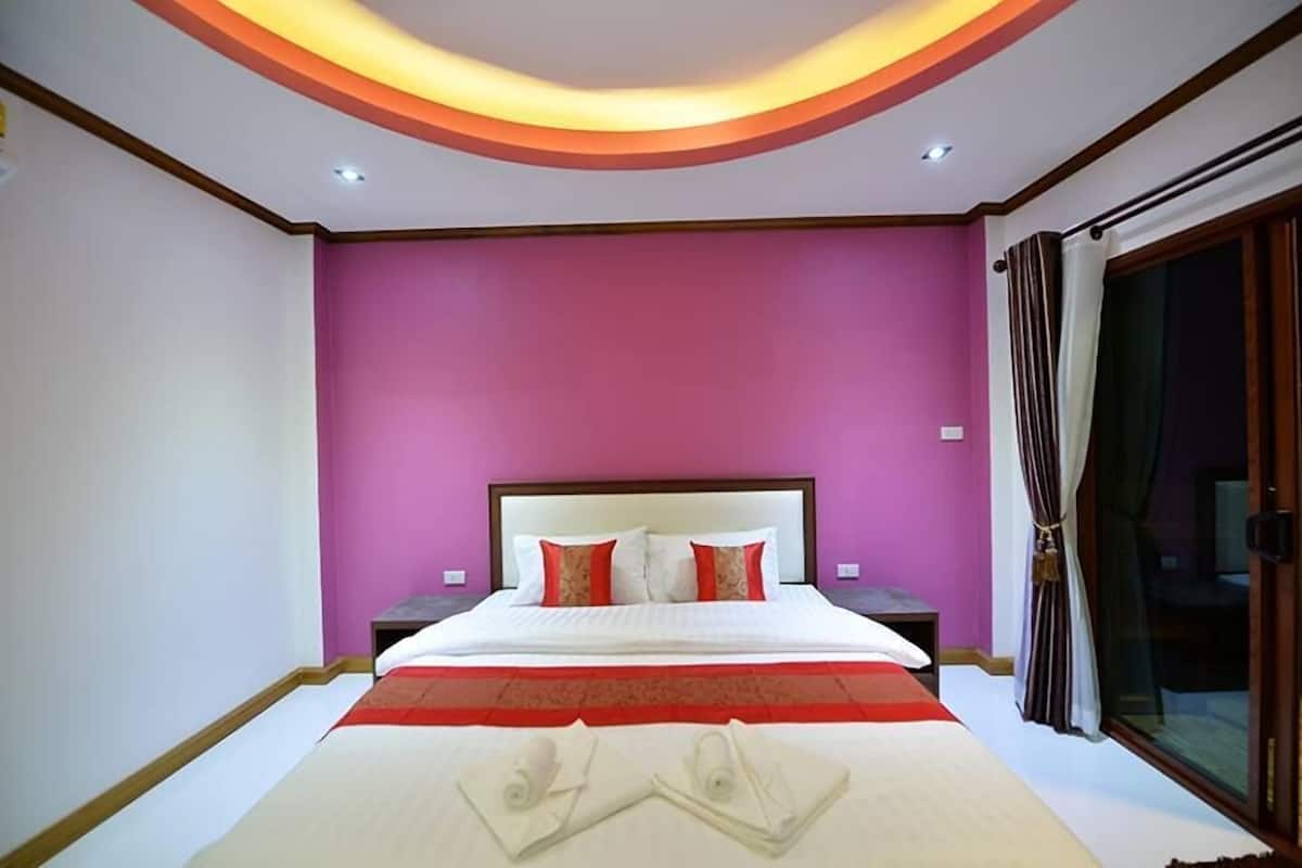 A bedroom with a bed, nightstands, a red and white bedspread, and a large window with curtains.