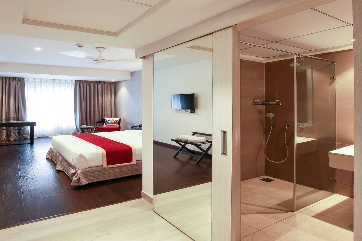 A modern hotel room with a large bed, a desk, a TV, and a walk-in shower.
