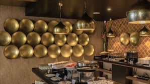 A buffet area with a wall of golden bowls, a variety of food items, and a counter with plates and cups. - Deccan Serai (Hyderabad)