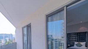 A modern hotel room with a balcony, a sliding glass door leading to a city view, and a neatly made bed with pillows. - Deccan Serai (Hyderabad)