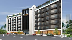 A modern hotel with a prominent AT HOME HOTEL sign, multiple balconies, and a parking area with cars. - Deccan Serai (Hyderabad)