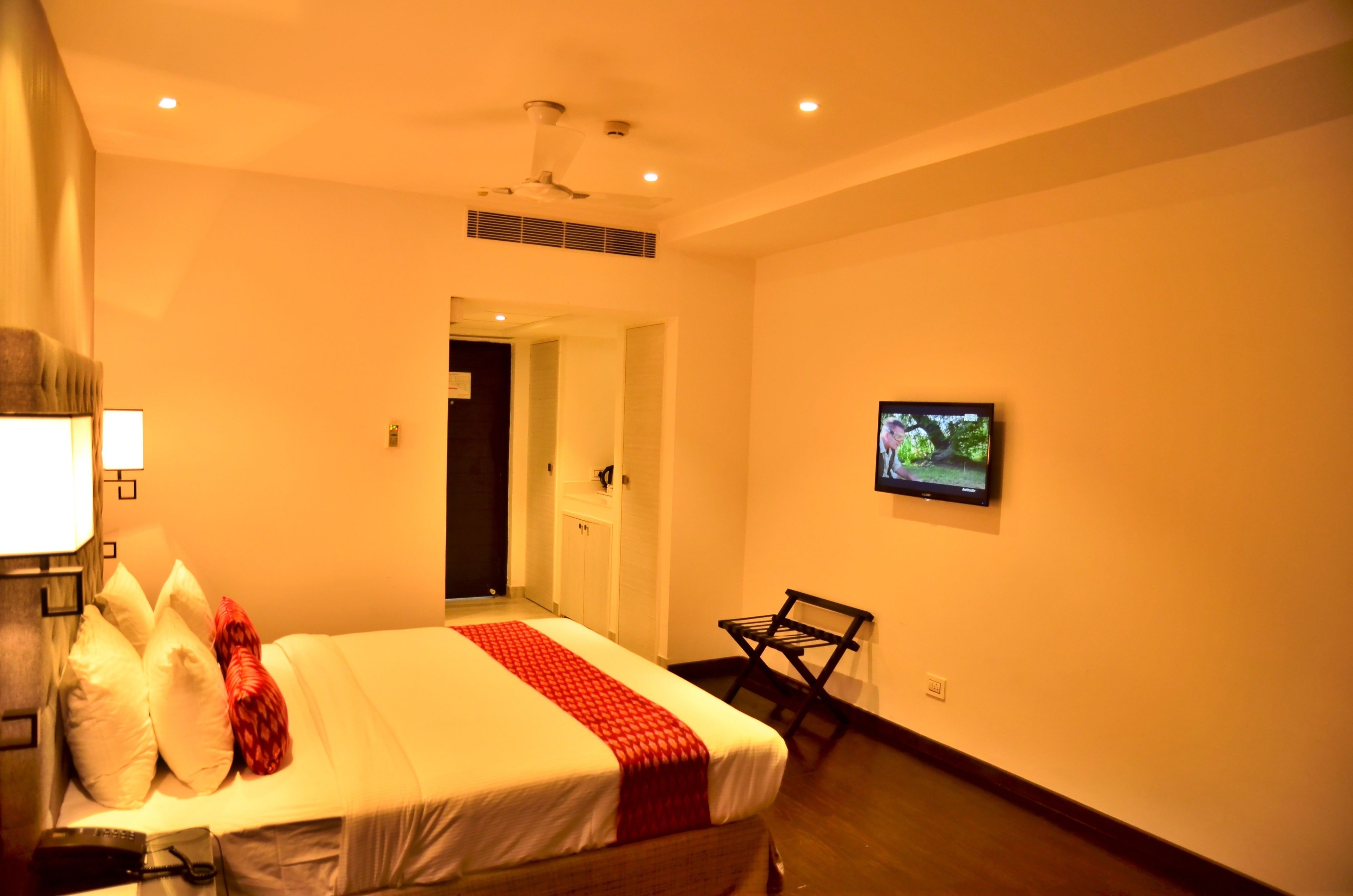 Une chambre d’hôtel équipée d’un lit, d’un téléviseur fixé au mur, d’une chaise et d’un ventilateur de plafond.