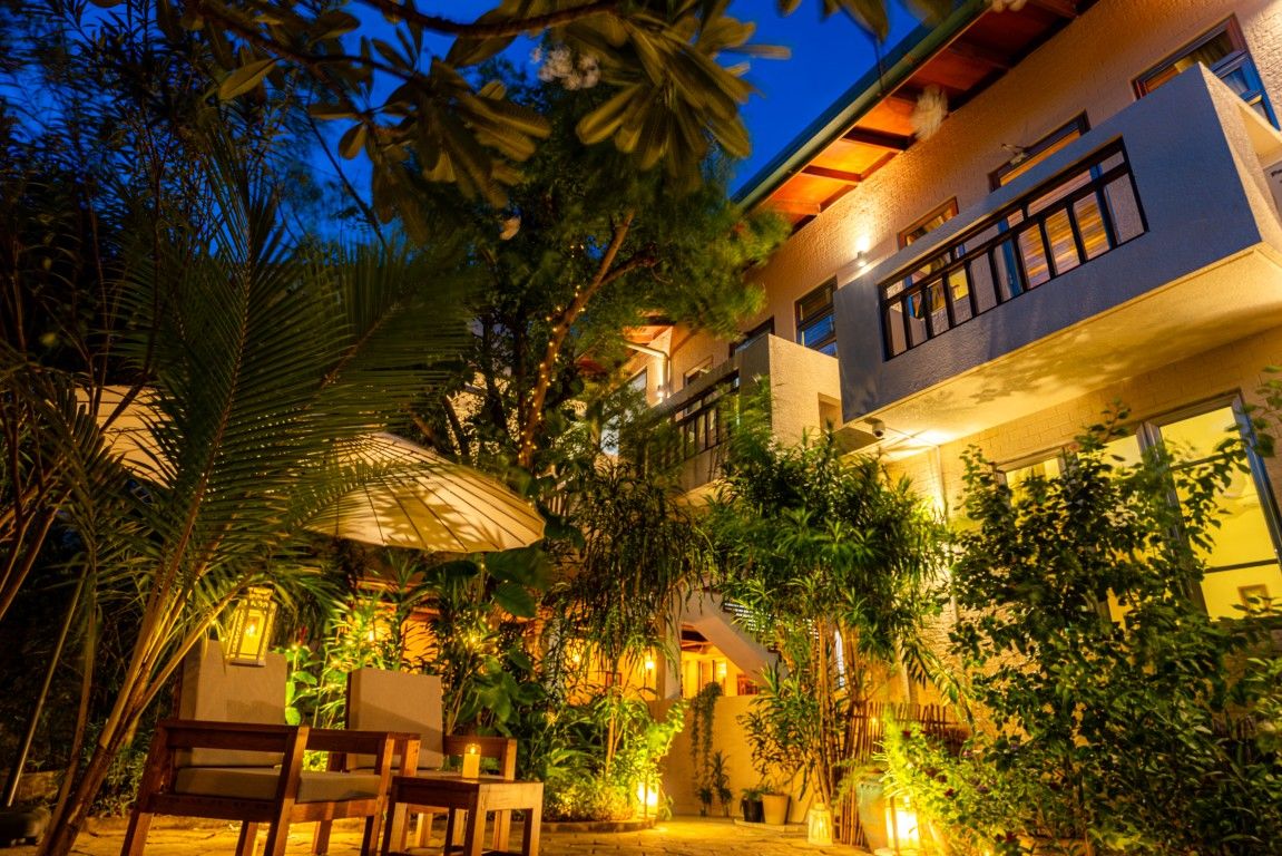 Un patio con zona de comedor, rodeado de exuberante vegetación y un edificio con balcón.