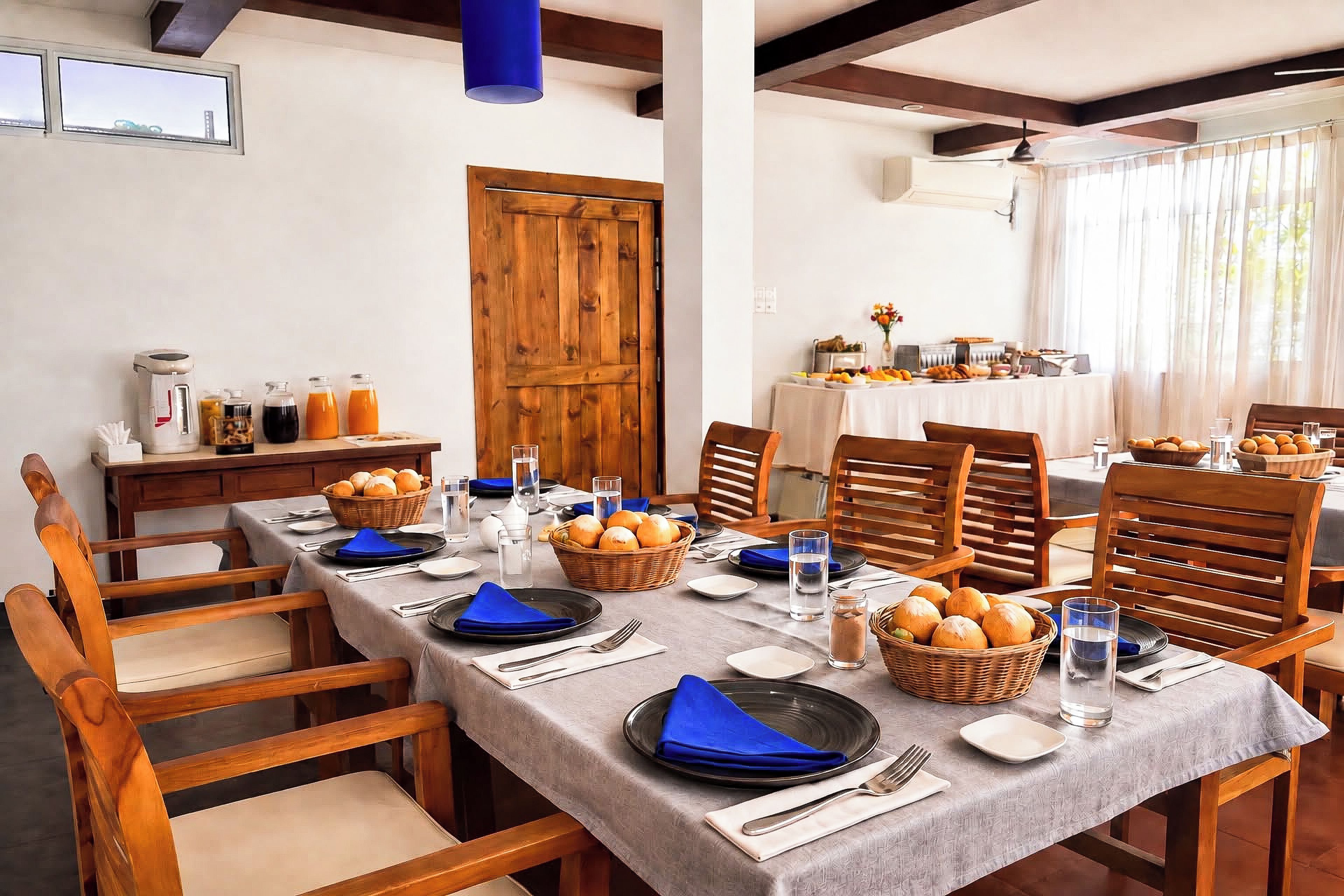A dining area with a long table set for a meal, wooden chairs, and a view of the outdoors.