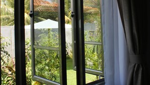 Ein Fenster mit Blick auf einen Garten, der verschiedene Pflanzen und einen weißen Sonnenschirm zeigt.