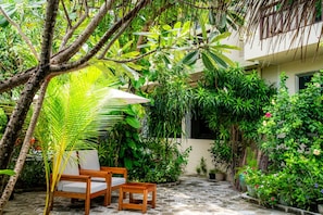 A patio area with a wooden chair and table, surrounded by lush greenery and a stone floor. - Cerulean View (Hanimaadhoo)