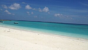 Ein Strand mit klarem türkisblauem Wasser, ein Boot am Ufer und eine entfernte Küstenlinie.