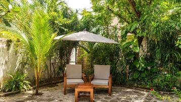 Un área de estar al aire libre con dos sillas y una mesa bajo una pérgola, rodeada de abundante vegetación.