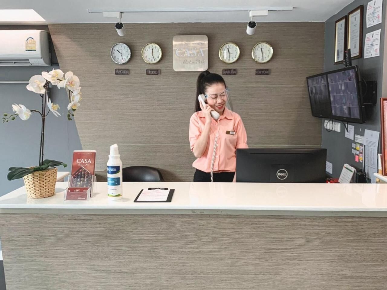 A reception desk with a receptionist, multiple clocks, a computer, and a monitor.