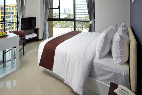 A hotel room with a large bed, a desk with a TV, and a view of the city through large windows. - Casa Residence Hotel (Bangkok)