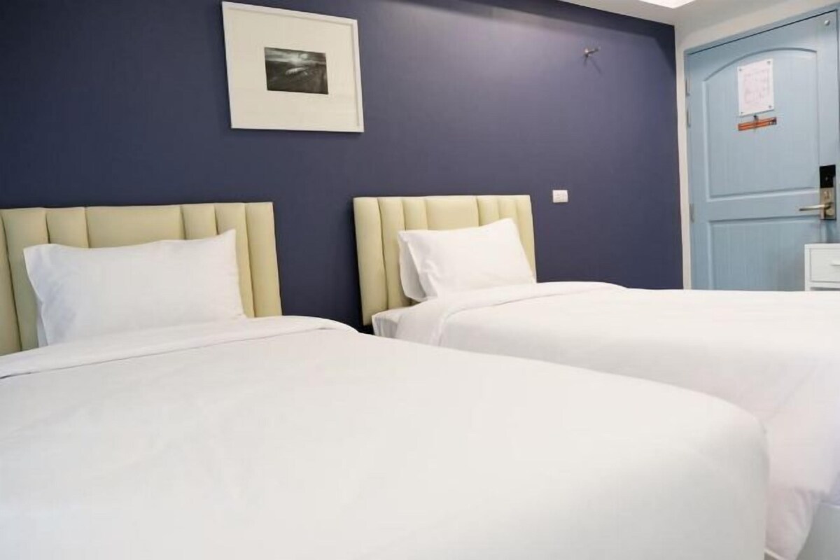 A hotel room with two beds, a framed picture on the wall, and a blue door.
