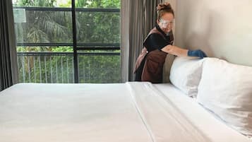 Ein Hotelzimmer mit einem großen Bett, einem Fenster mit Blick auf Grünflächen und einer Person, die die Bettdecke zurechtzieht.