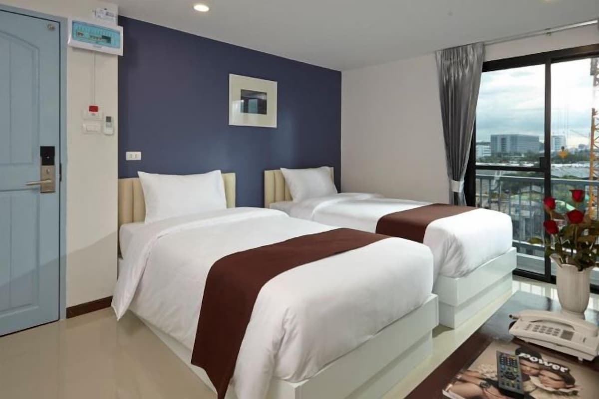 Habitación de hotel con dos camas, un escritorio con teléfono y ventana con vista a edificios.