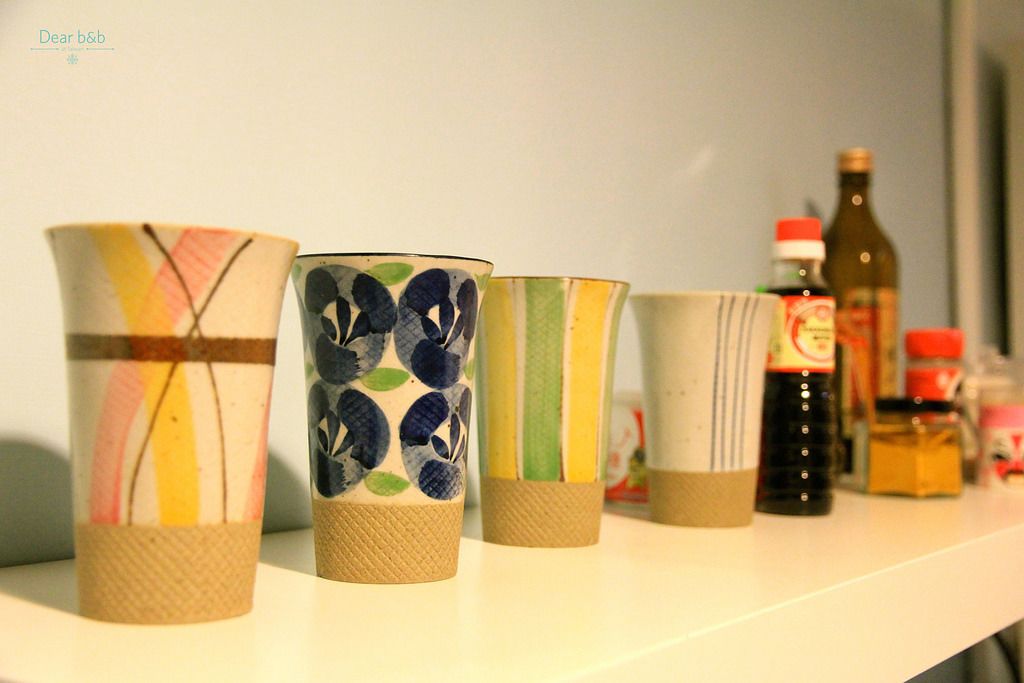 Four ceramic cups with different patterns on a shelf.